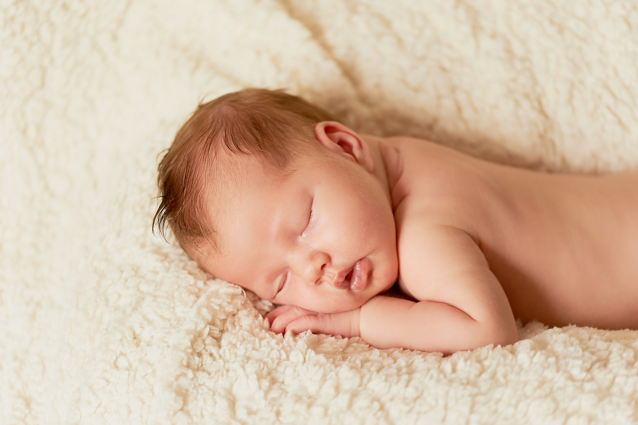 The baby, newly born, lies on the plaid and sleeping